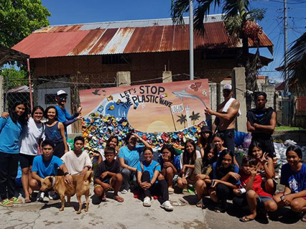 A group of people taking a photo in front of a Let's Stop Plastic Waste mural.